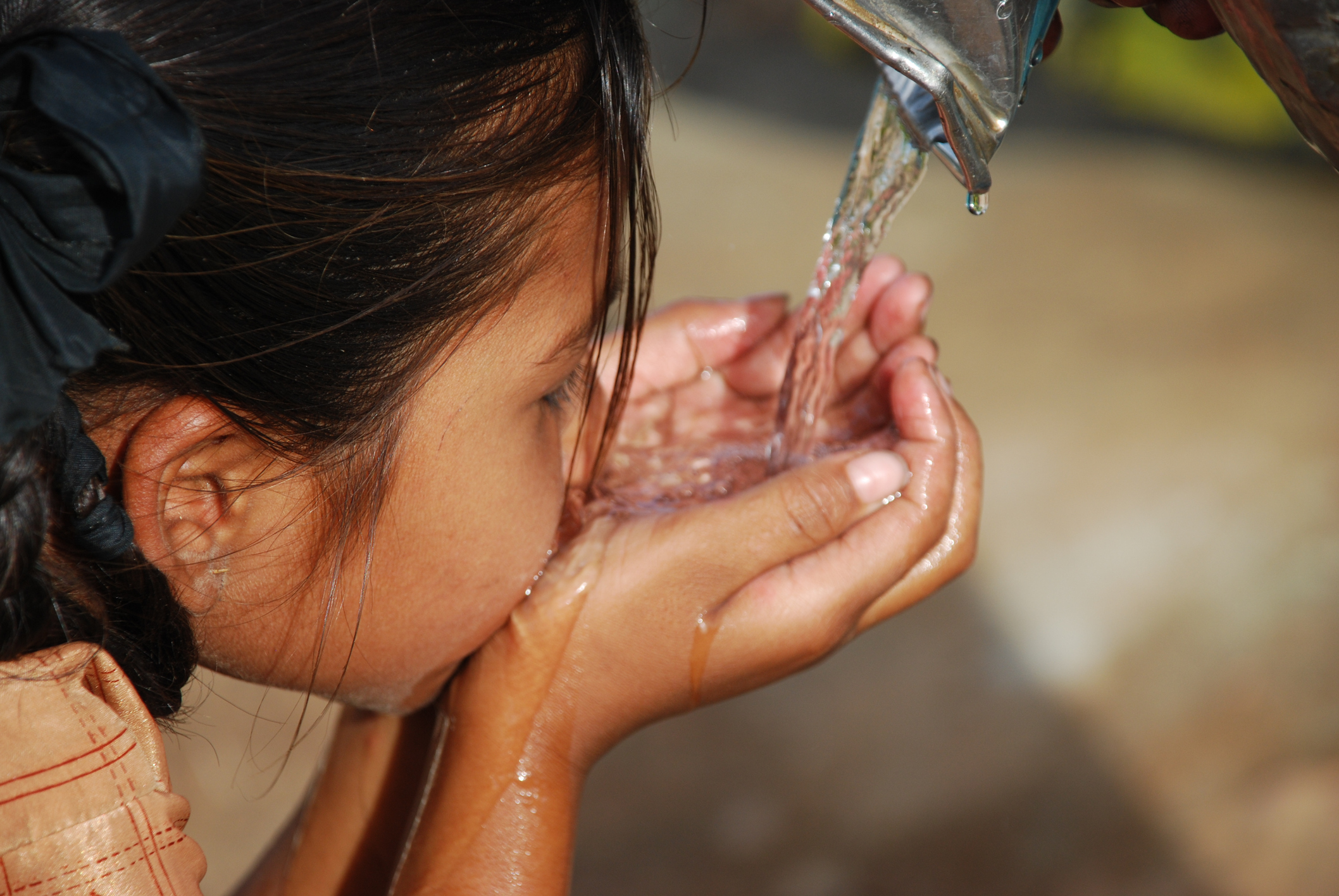 Petit enfant aux cheveux noirs buvant de l'eau à l'aide de ses mains