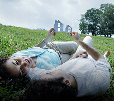Deux personnes allongées dans la pelouse tiennent un papier découpé en forme de maison.